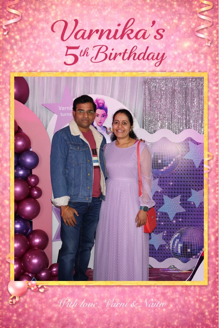 A man and woman pose together at Varnikas 5th Birthday party with pink balloon decorations and glittery backdrop