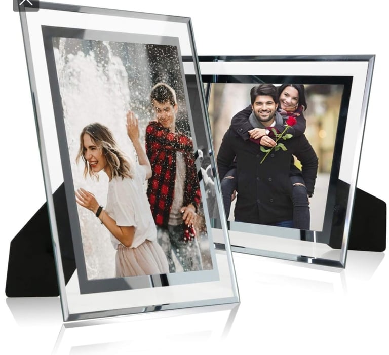 Two modern silver and black photo frames displaying family photos, angled on reflective surface