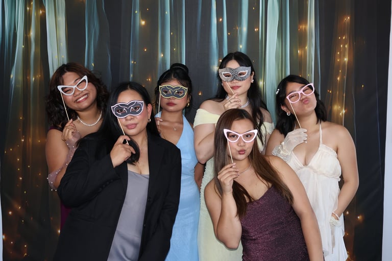 Group of six women wearing decorative eyeglasses posing together in front of a sparkly backdrop at a party